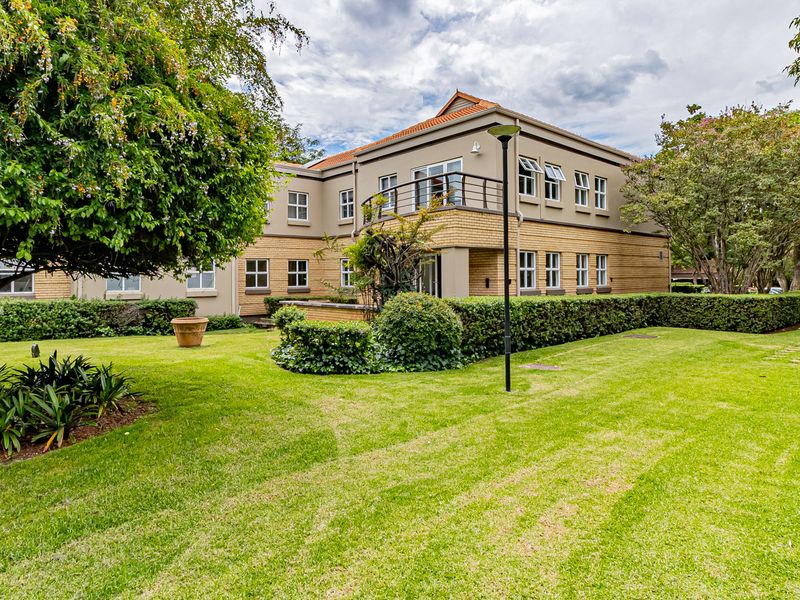 A well-maintained two-story office building exterior featuring brick facade, balcony, and landscaped garden surroundings.