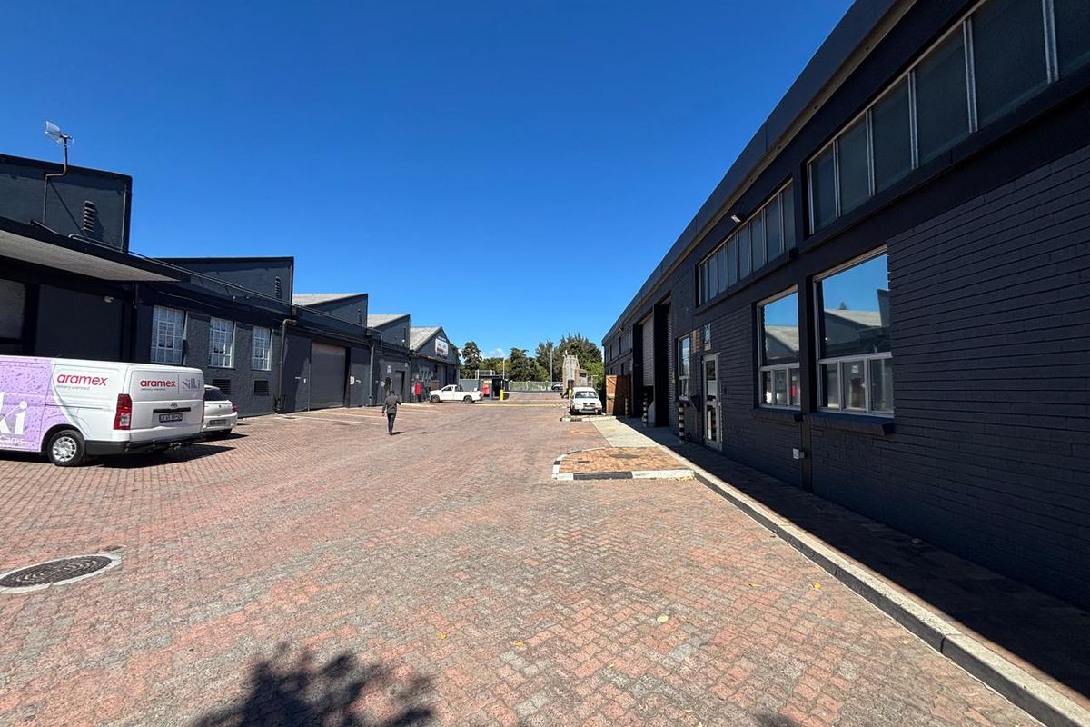 Exterior view of an industrial complex featuring paved driveway access, dark brick facade, and large windows.