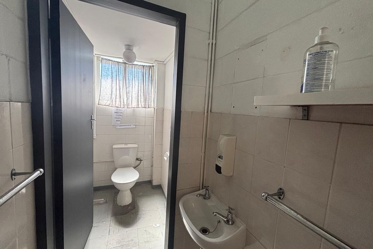 A functional industrial-style restroom featuring a wall-mounted basin, tiled walls, and a separate toilet cubicle with basic fixtures.