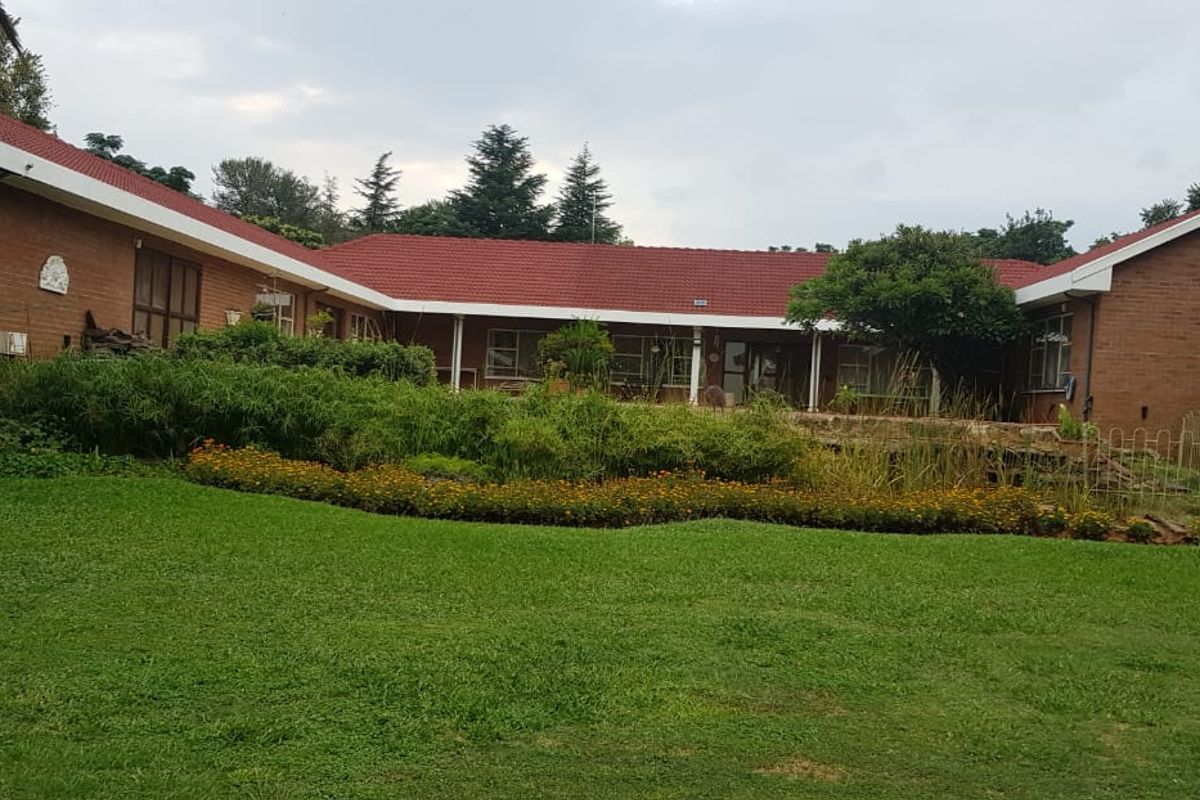 A view of the rear exterior of the brick-built small holding, featuring a large lawn, established garden beds, and a covered patio area.