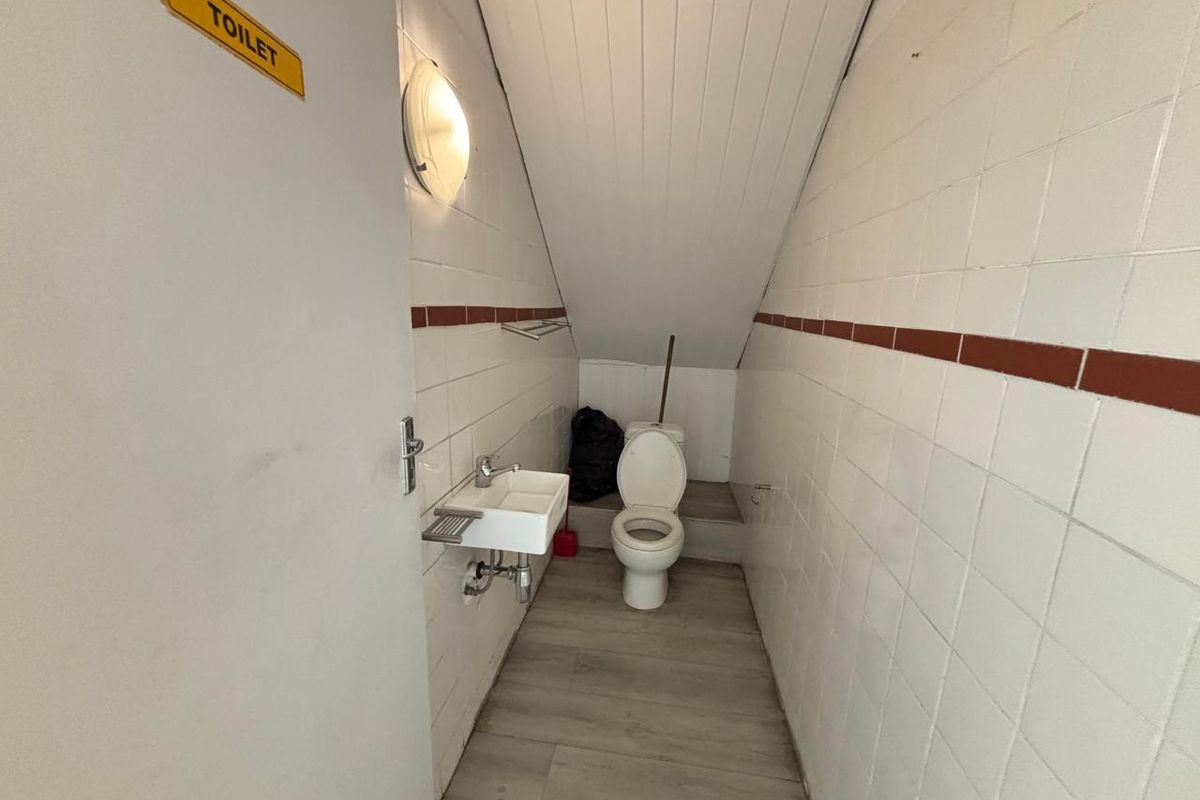 A compact office restroom featuring a wall-mounted basin, toilet, and tiled walls under a sloped ceiling.