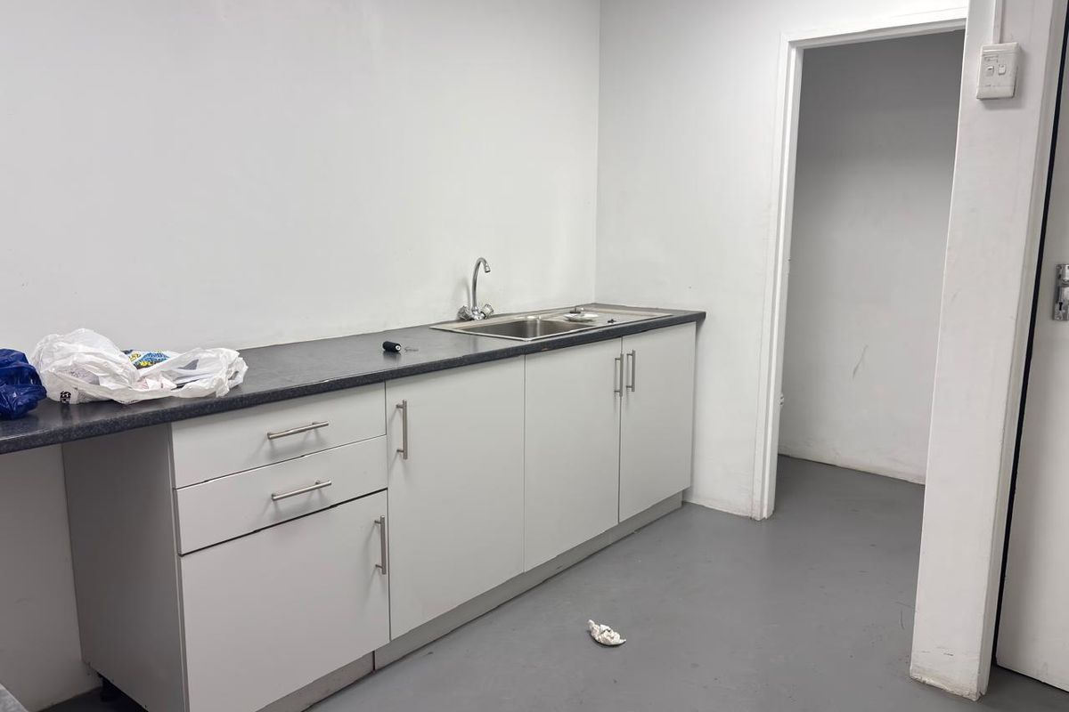 A functional office kitchenette featuring white cabinetry, a dark laminate countertop, and a stainless steel sink with a chrome faucet.