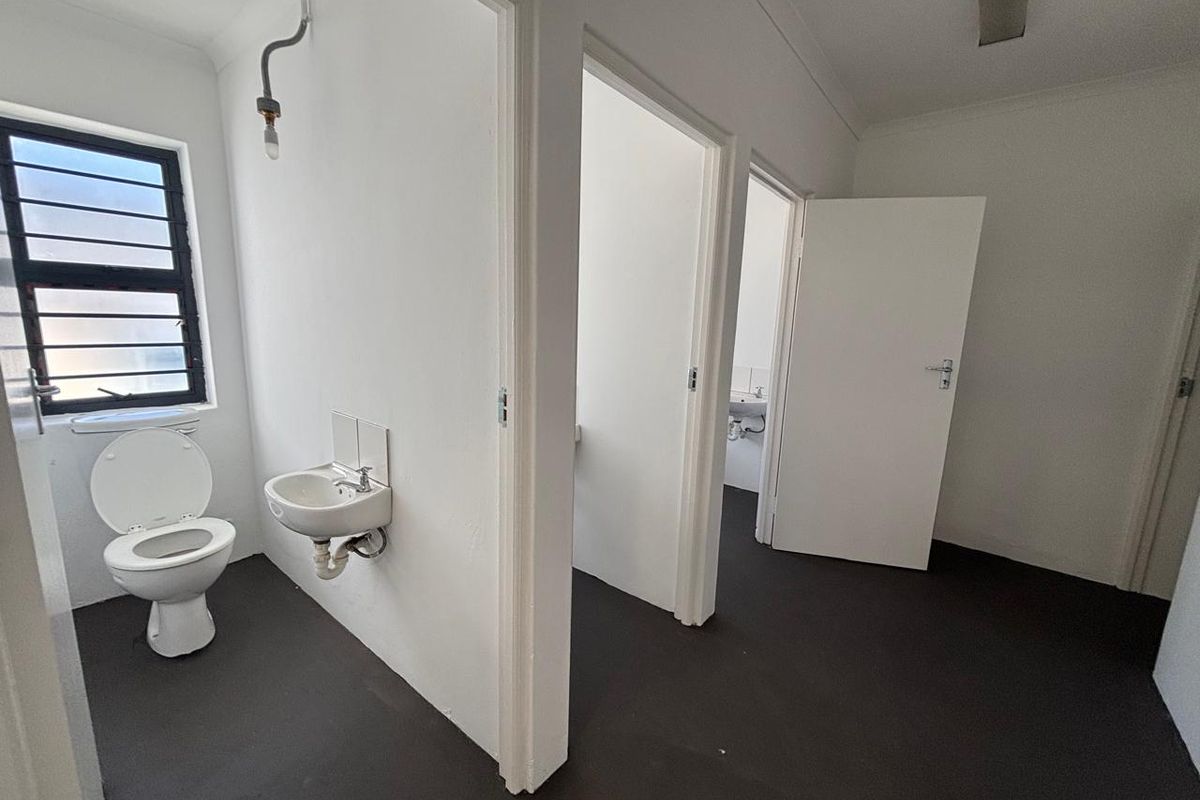 A functional industrial restroom area featuring a wall-mounted basin, toilet, and multiple partitioned cubicles with simple finishes.
