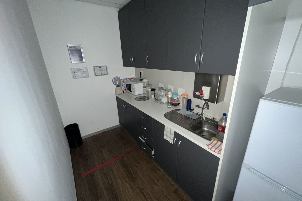 A compact office kitchenette featuring dark grey cabinetry, a stainless steel sink, and wood-look flooring.