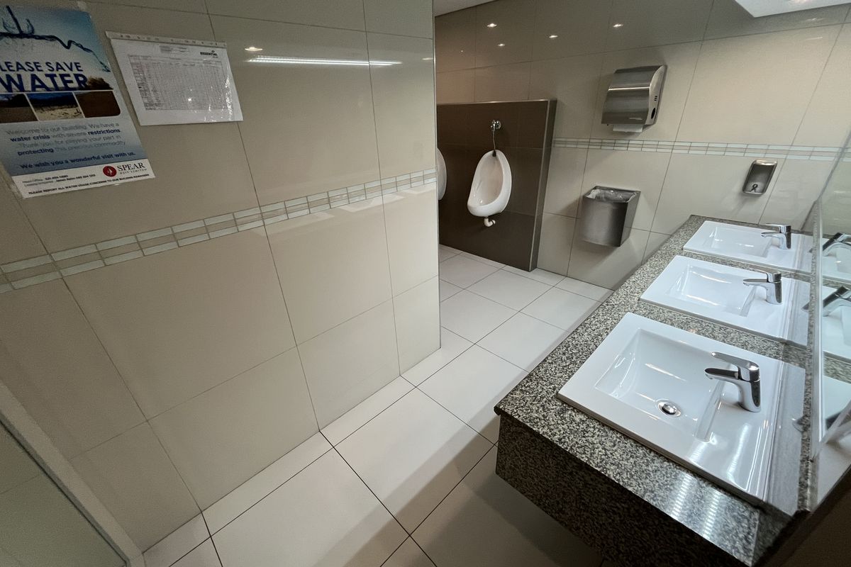 A clean, modern commercial restroom featuring multiple vanity basins with granite countertops, wall-mounted urinals, and tiled wall and floor finishes.