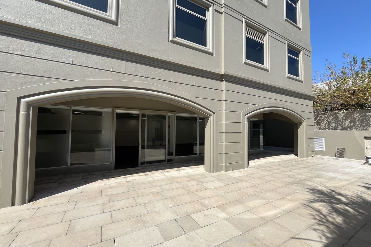 Ground floor office space with a paved patio area, featuring arched architectural detailing and large glass sliding doors for natural light.