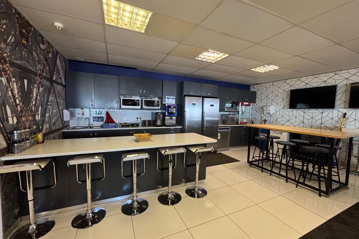 Modern office kitchen and breakroom area featuring dark cabinetry, integrated appliances, a breakfast bar, and tiled flooring.