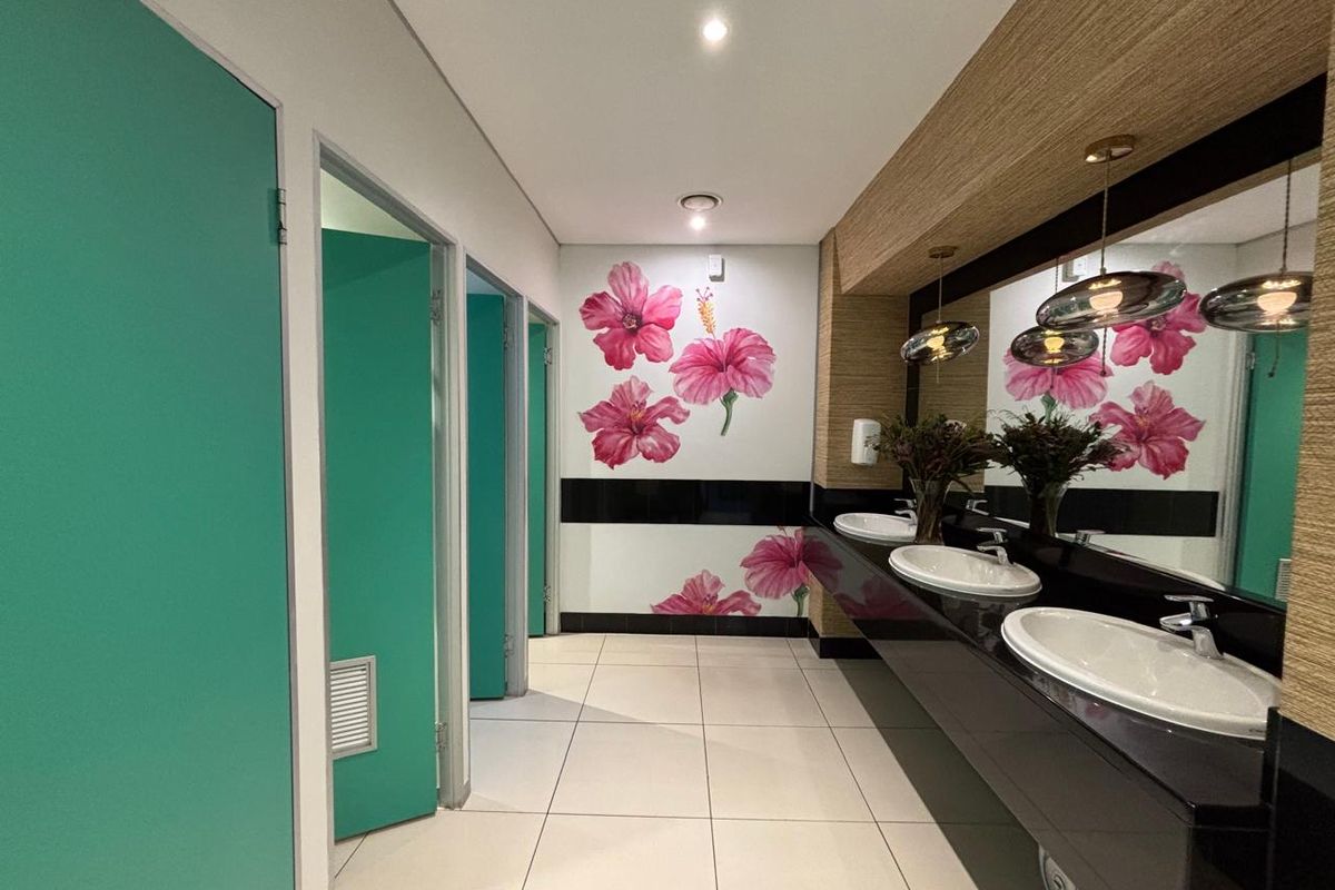 Modern office restroom featuring a long vanity with three integrated sinks, large mirrors, and multiple private cubicles with teal doors.