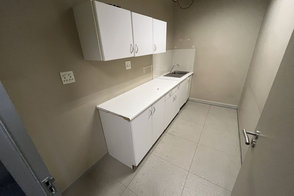 A small office kitchenette featuring white cabinetry, a single basin sink, and tiled flooring, currently requiring maintenance and ceiling repairs.