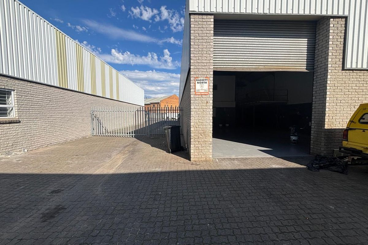 Industrial warehouse exterior featuring a paved yard, secure perimeter fencing, and a large roller shutter door entrance.