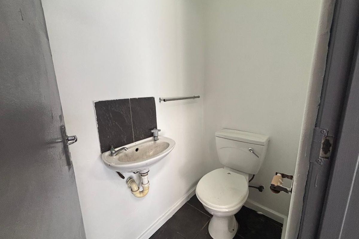A compact industrial-style restroom featuring a wall-mounted washbasin and a standard toilet with dark floor tiling.