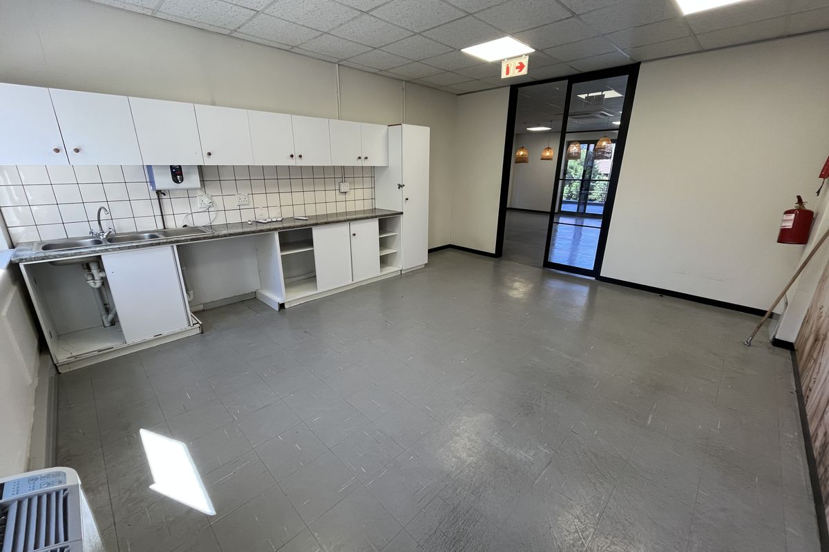 A functional office kitchenette featuring white cabinetry, a stainless steel sink, tiled backsplash, and a suspended ceiling with recessed lighting.