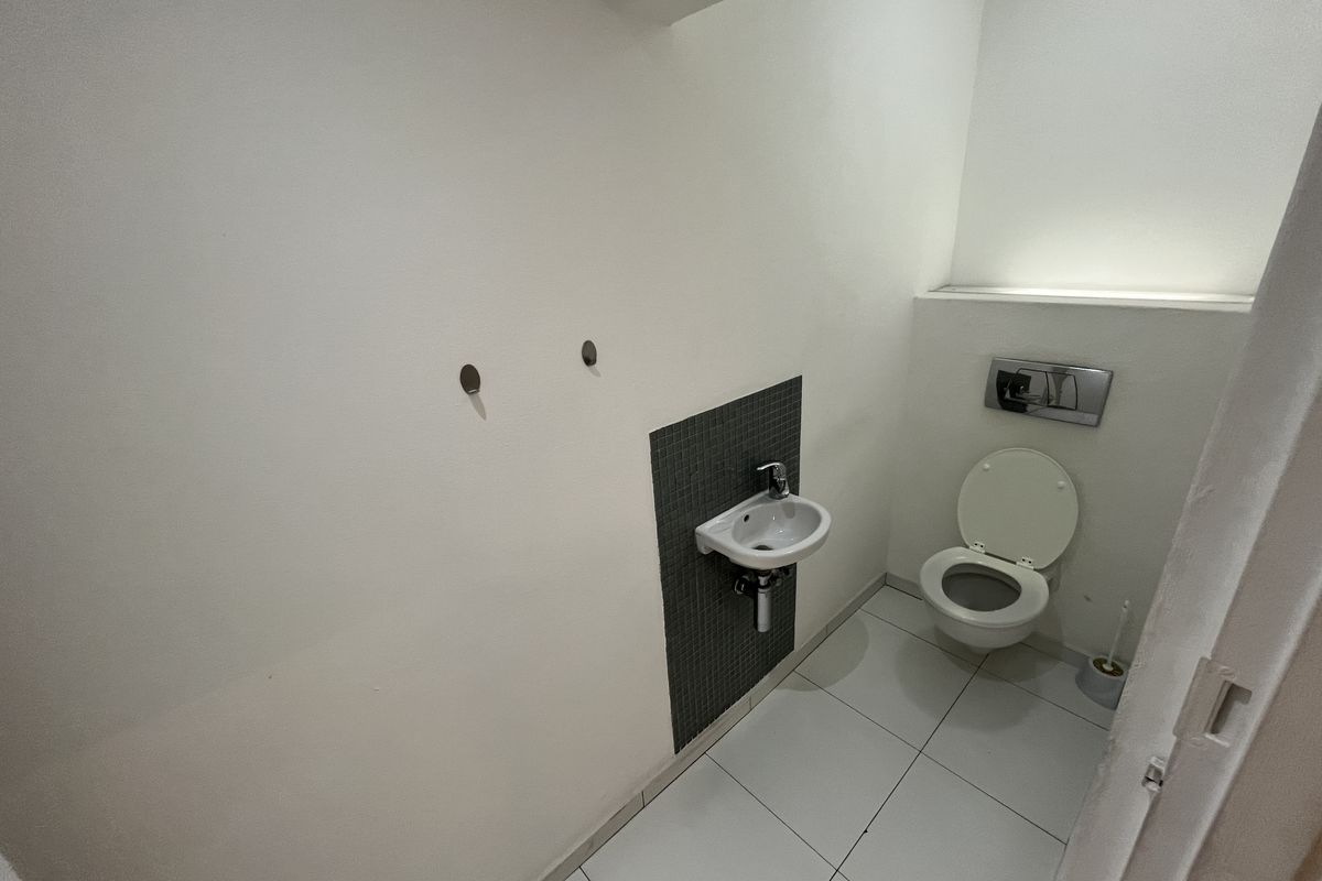 A compact office restroom featuring a wall-mounted toilet with a concealed cistern and a small wall-mounted basin with mosaic tile splashback.