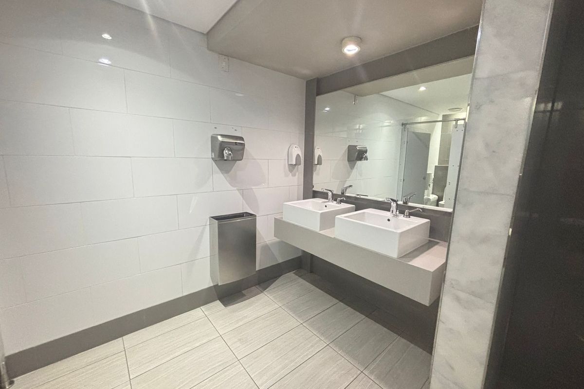 Modern office restroom featuring a dual-basin vanity with integrated mirrors, tiled walls, and stainless steel fixtures.