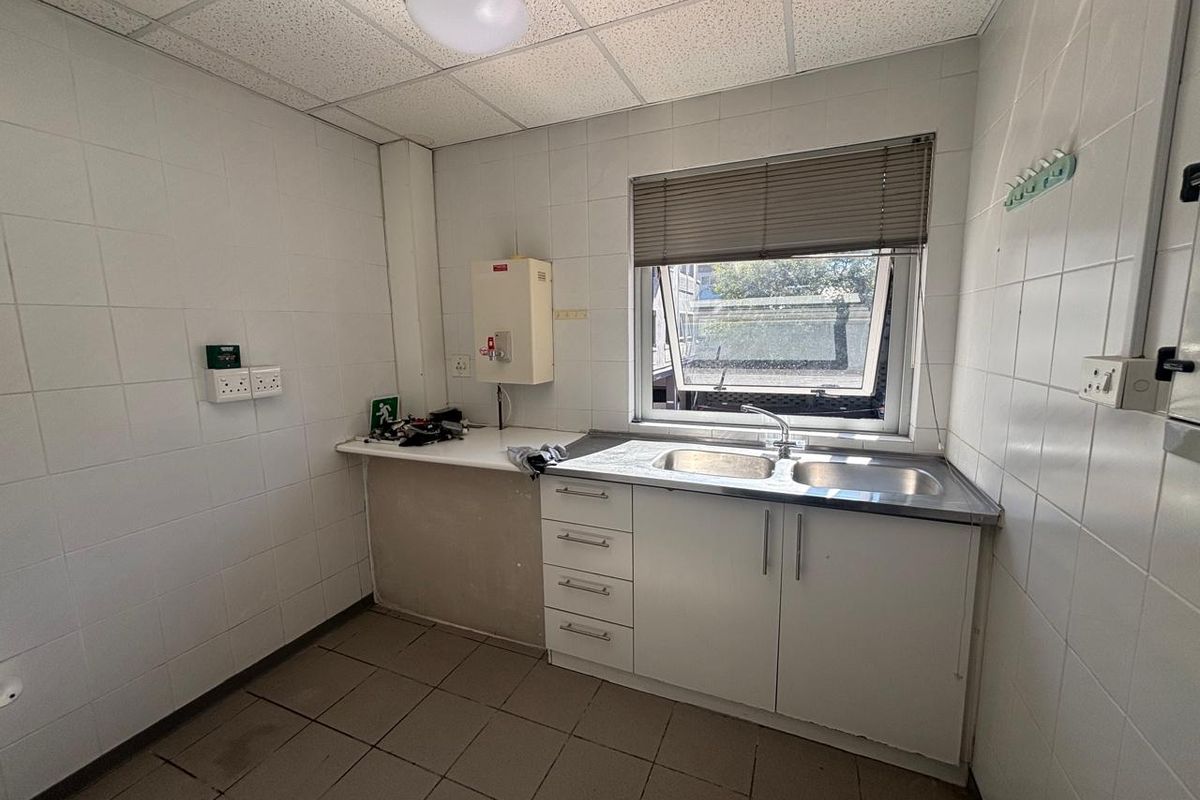 A functional office kitchenette featuring a stainless steel double sink, built-in cabinetry, tiled walls, and a drop ceiling with integrated lighting.