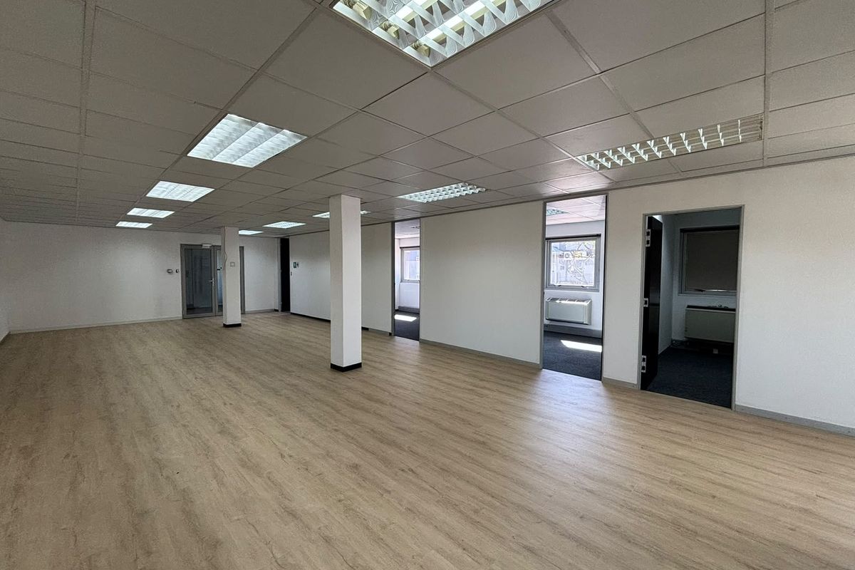 Spacious open-plan office area featuring modern laminate flooring, suspended ceilings with recessed lighting, and multiple access points to adjacent rooms.