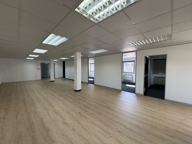 Spacious open-plan office area featuring modern laminate flooring, suspended ceilings with recessed lighting, and multiple access points to adjacent rooms.
