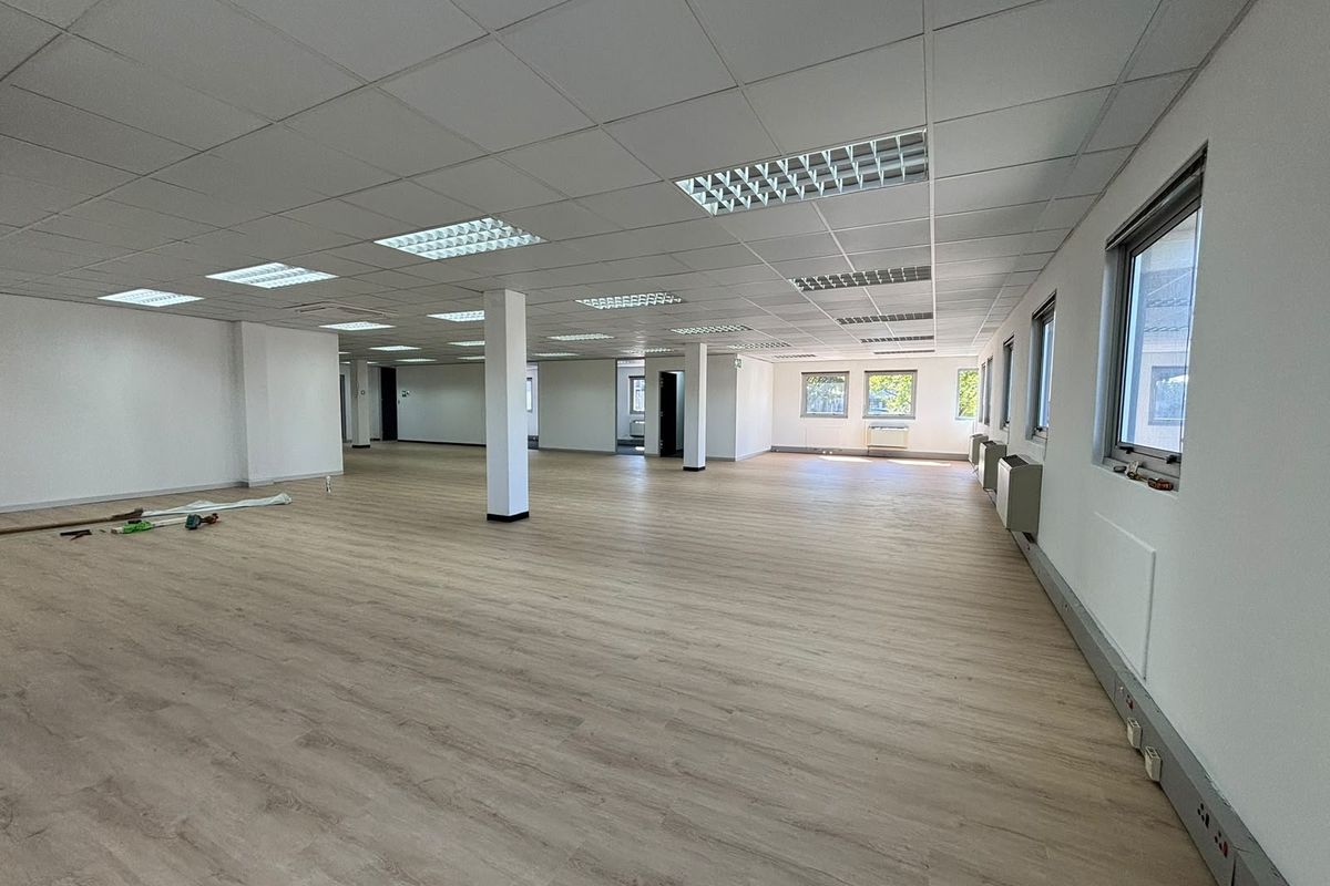 A spacious, open-plan office area featuring modern laminate flooring, suspended ceilings with recessed lighting, and perimeter trunking for flexible workstation configuration.