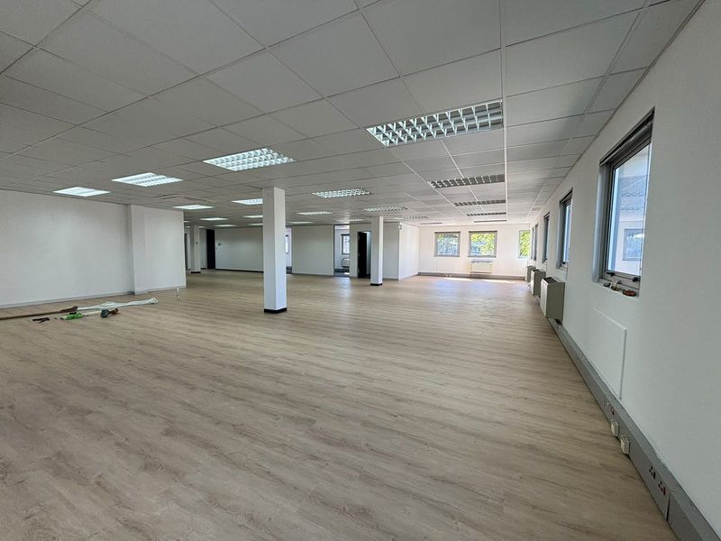 A spacious, open-plan office area featuring modern laminate flooring, suspended ceilings with recessed lighting, and perimeter trunking for flexible workstation configuration.