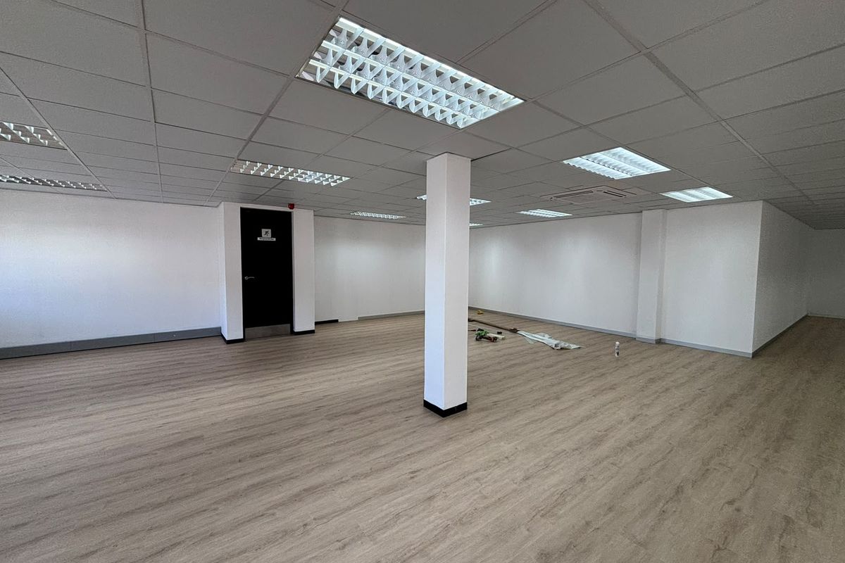A spacious, open-plan office area featuring modern laminate flooring, a clean suspended ceiling with recessed lighting, and a central structural column.