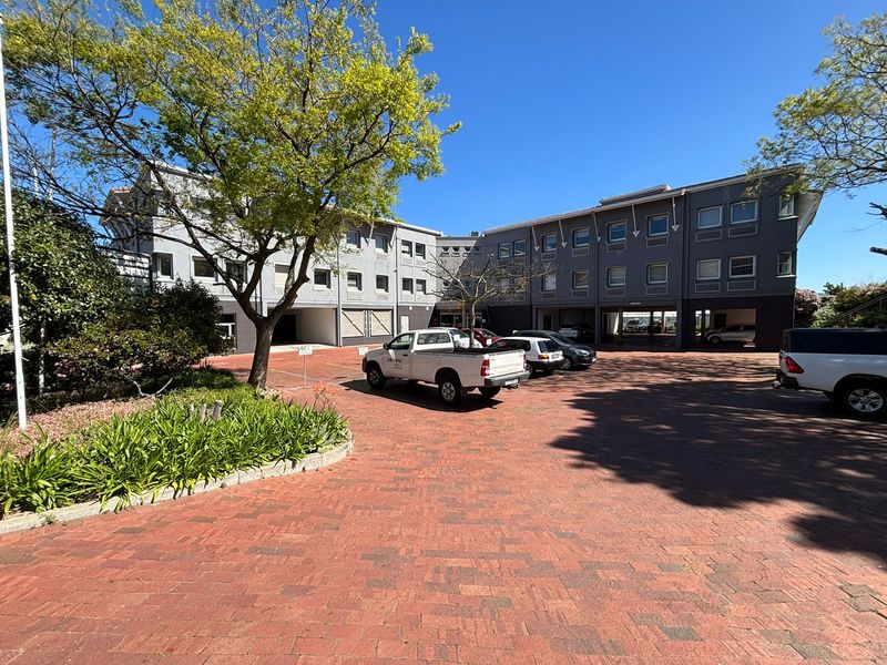 Exterior view of a multi-story office building featuring a paved driveway, covered parking bays, and established landscaping.