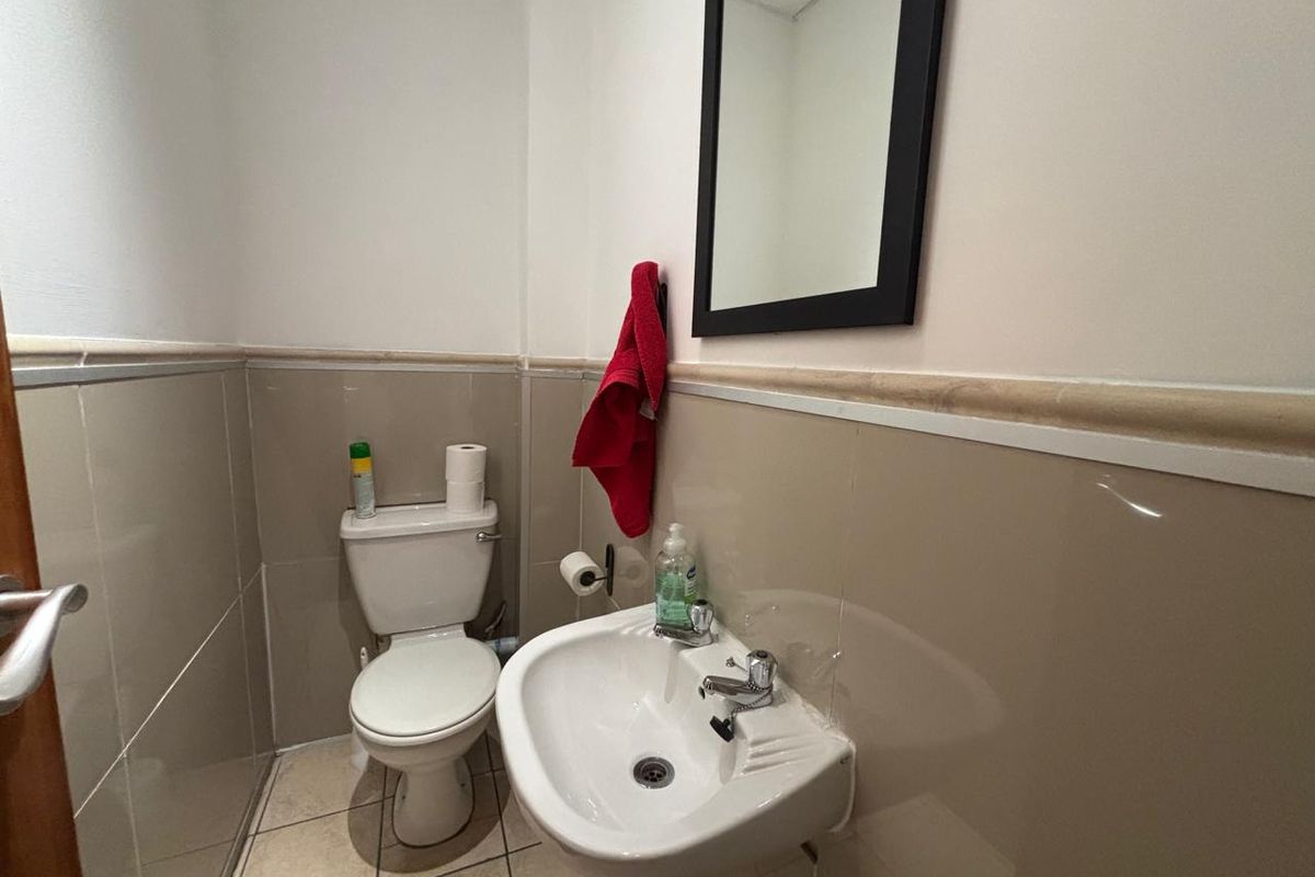 A compact office restroom featuring ceramic wall tiling, a pedestal sink, and a standard toilet suite.