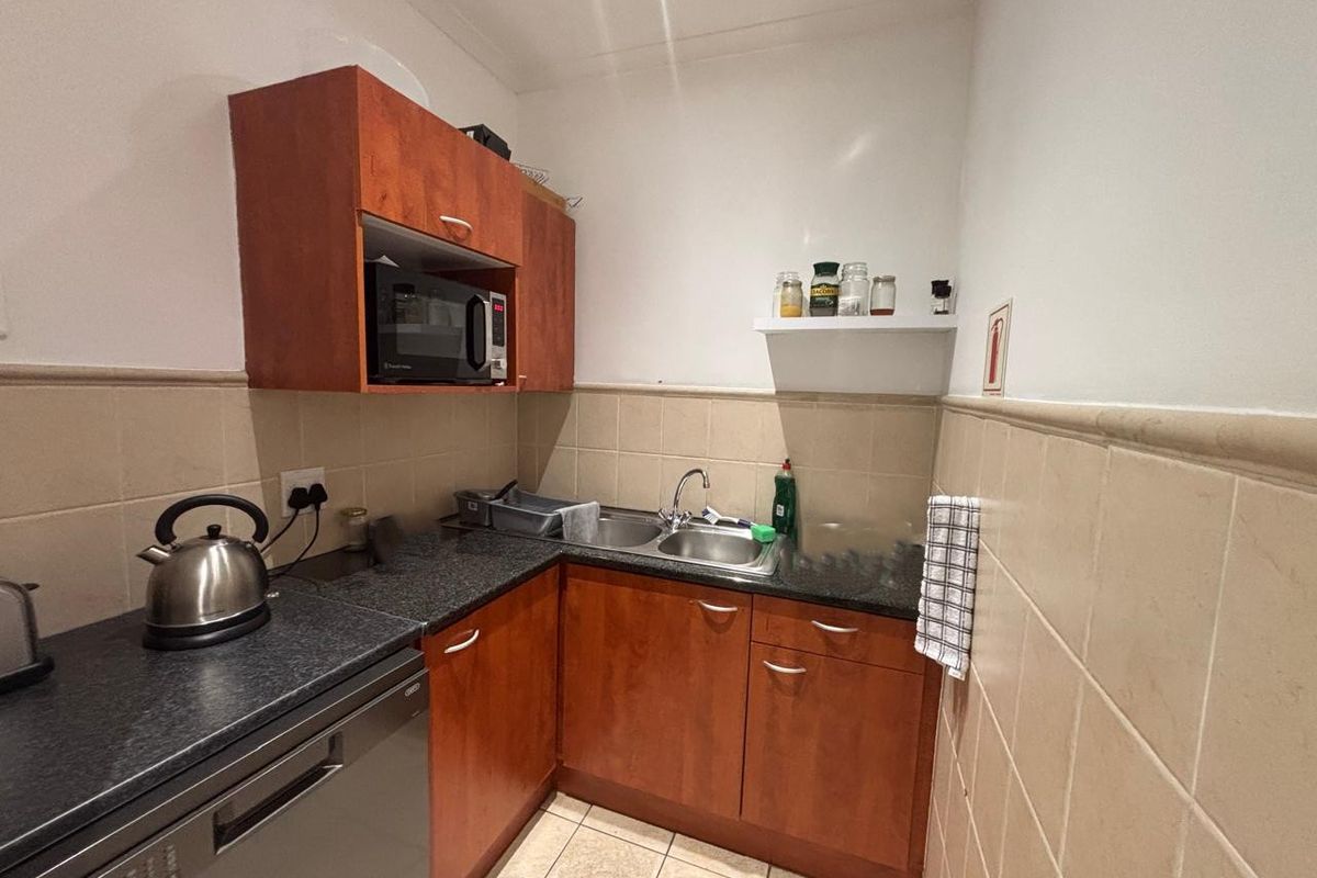 Compact office kitchenette featuring wood-veneer cabinetry, dark laminate countertops, stainless steel sink, and tiled backsplash.