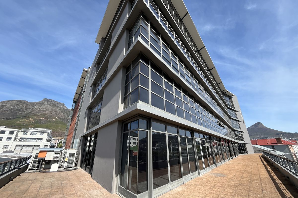 A modern multi-story office building exterior featuring extensive glass curtain walling and a spacious tiled terrace area with mountain views.