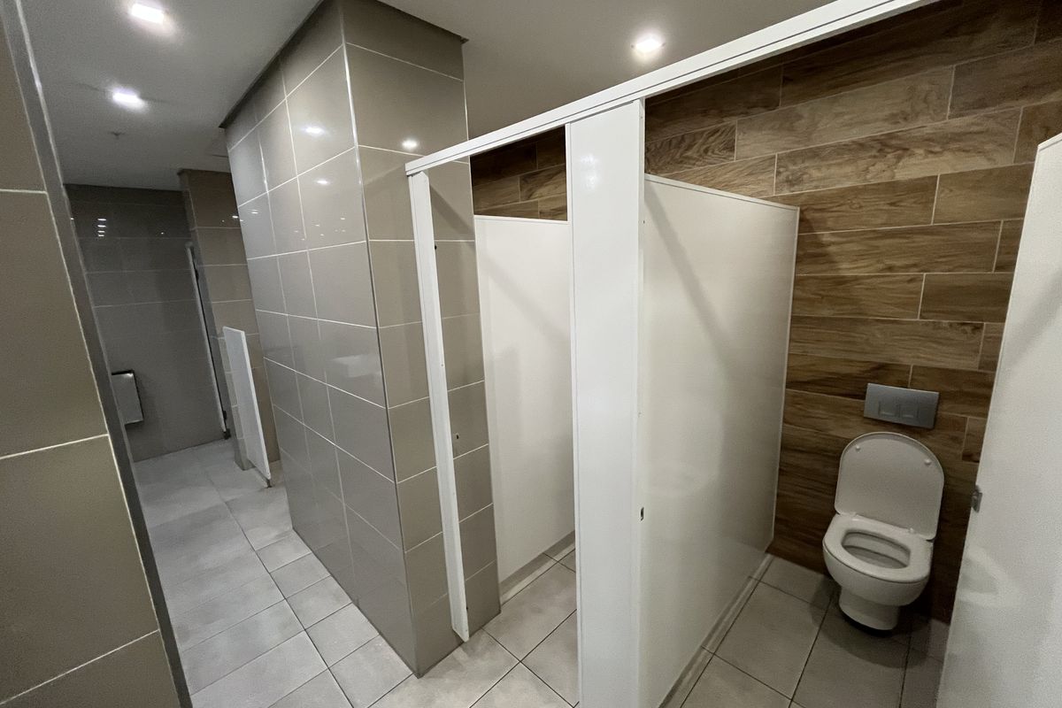Modern office restroom facility featuring tiled walls, wood-look accent tiling, and private toilet cubicles with wall-mounted flush plates.