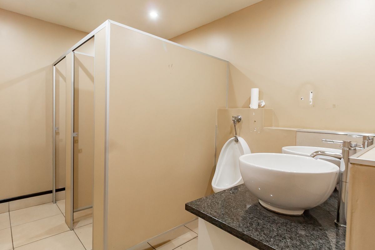 A functional office restroom featuring a granite vanity top with vessel sinks, a wall-mounted urinal, and partitioned toilet cubicles.