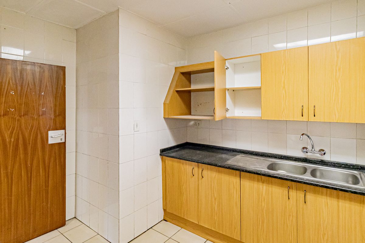 A functional office kitchenette featuring light wood cabinetry, a dark laminate countertop, a stainless steel double sink, and full-height wall tiling.