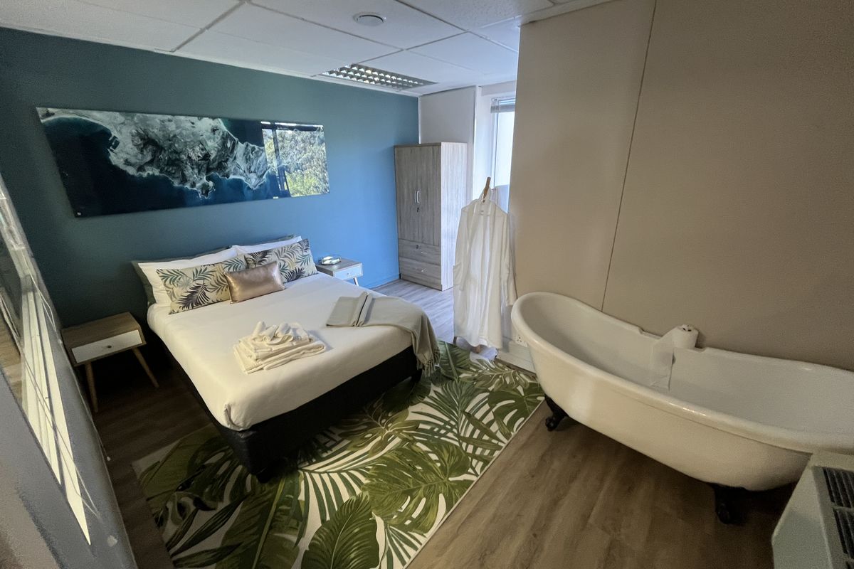 A bedroom suite featuring a freestanding clawfoot bathtub, wood-look flooring, and a blue accent wall with integrated lighting.