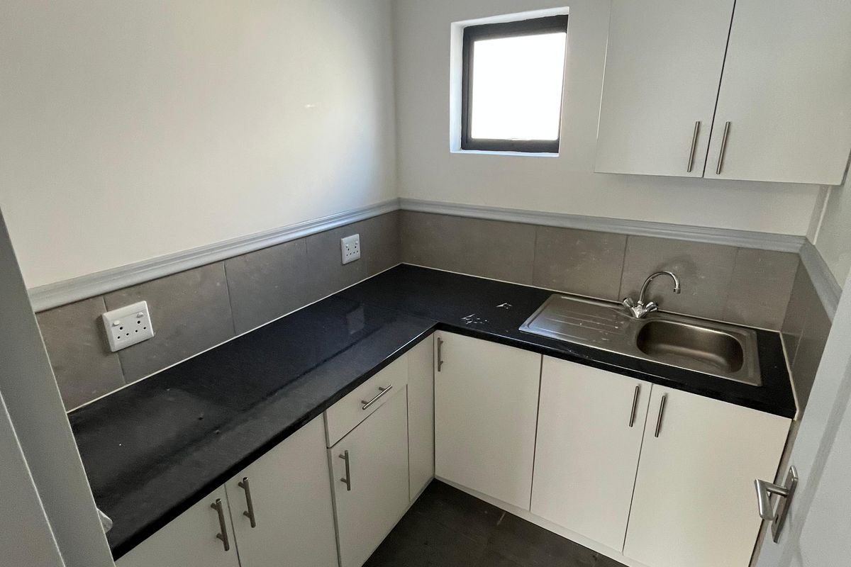 Compact kitchenette featuring white cabinetry, dark stone countertops, stainless steel sink, and tiled backsplash in a clean, functional industrial space.