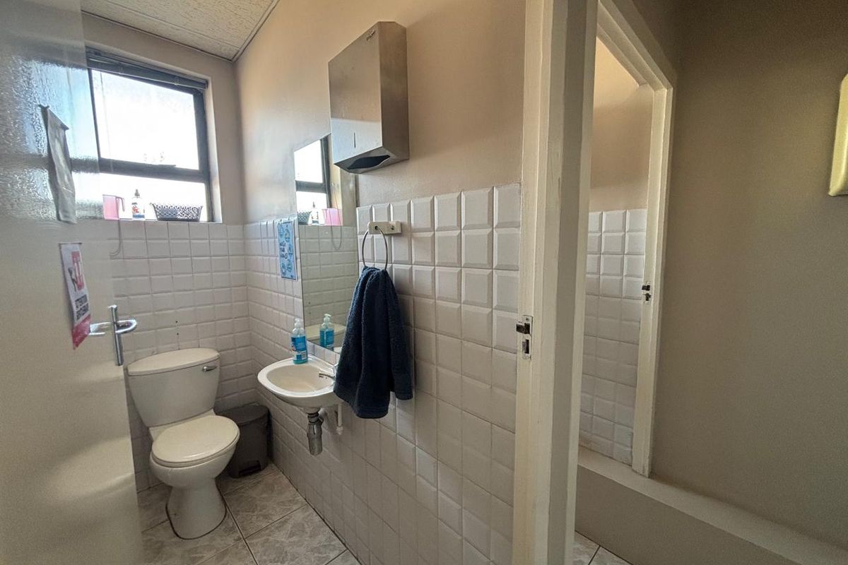 A functional office restroom featuring a standard toilet, wall-mounted basin, tiled walls, and tiled flooring with an adjacent stall.