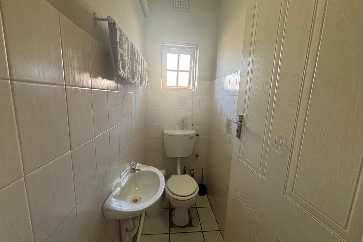 A compact office restroom featuring a wall-mounted basin, standard toilet, and tiled walls and flooring.