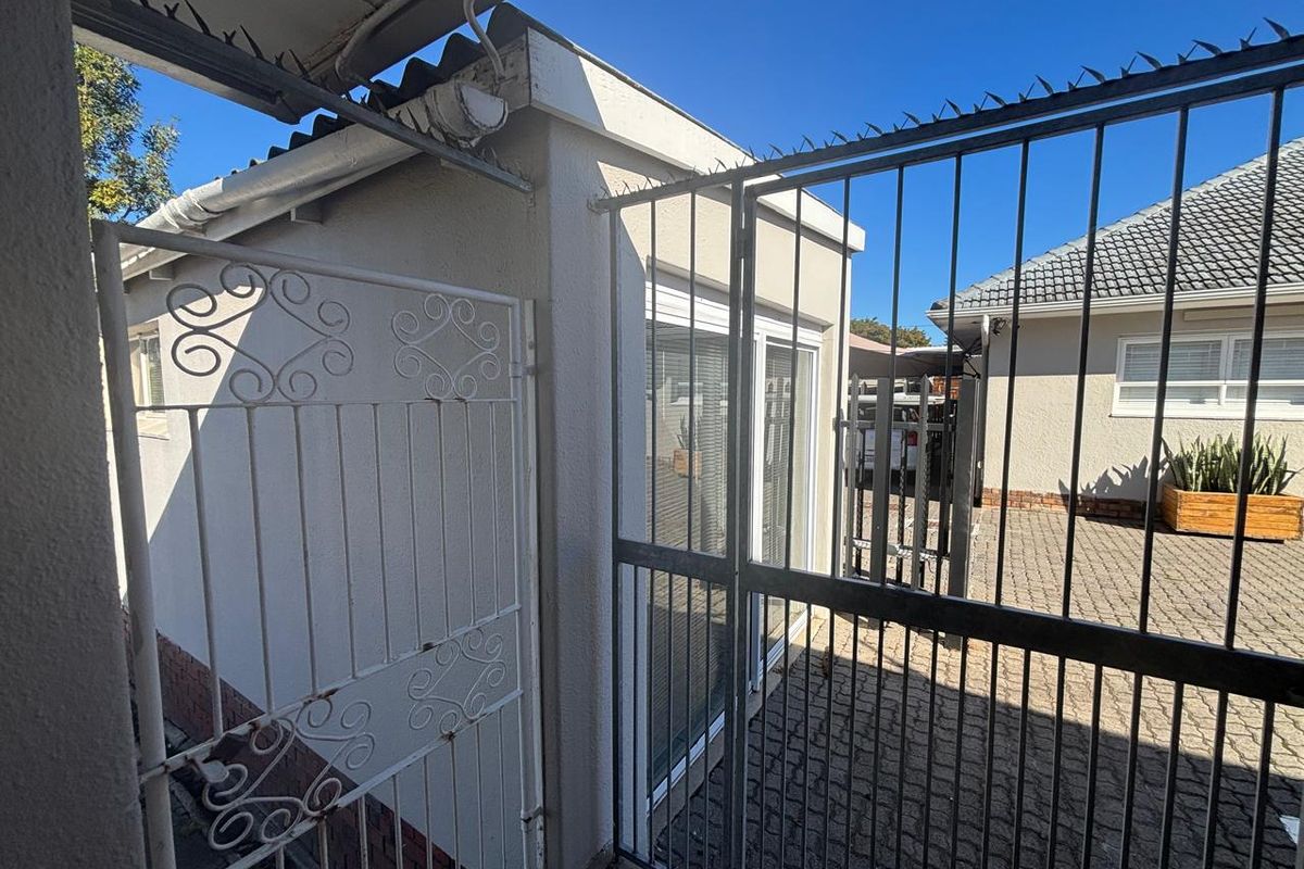 Exterior view of the office building entrance featuring a paved courtyard, secure metal gates, and sliding glass doors.