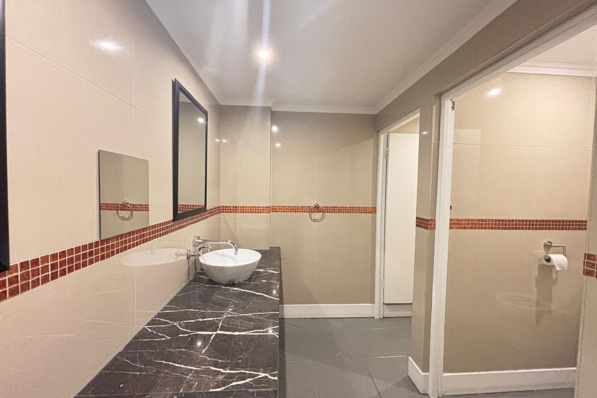 A clean, modern bathroom featuring a dark marble vanity top, a white vessel sink, and neutral wall tiling with a decorative mosaic accent border.