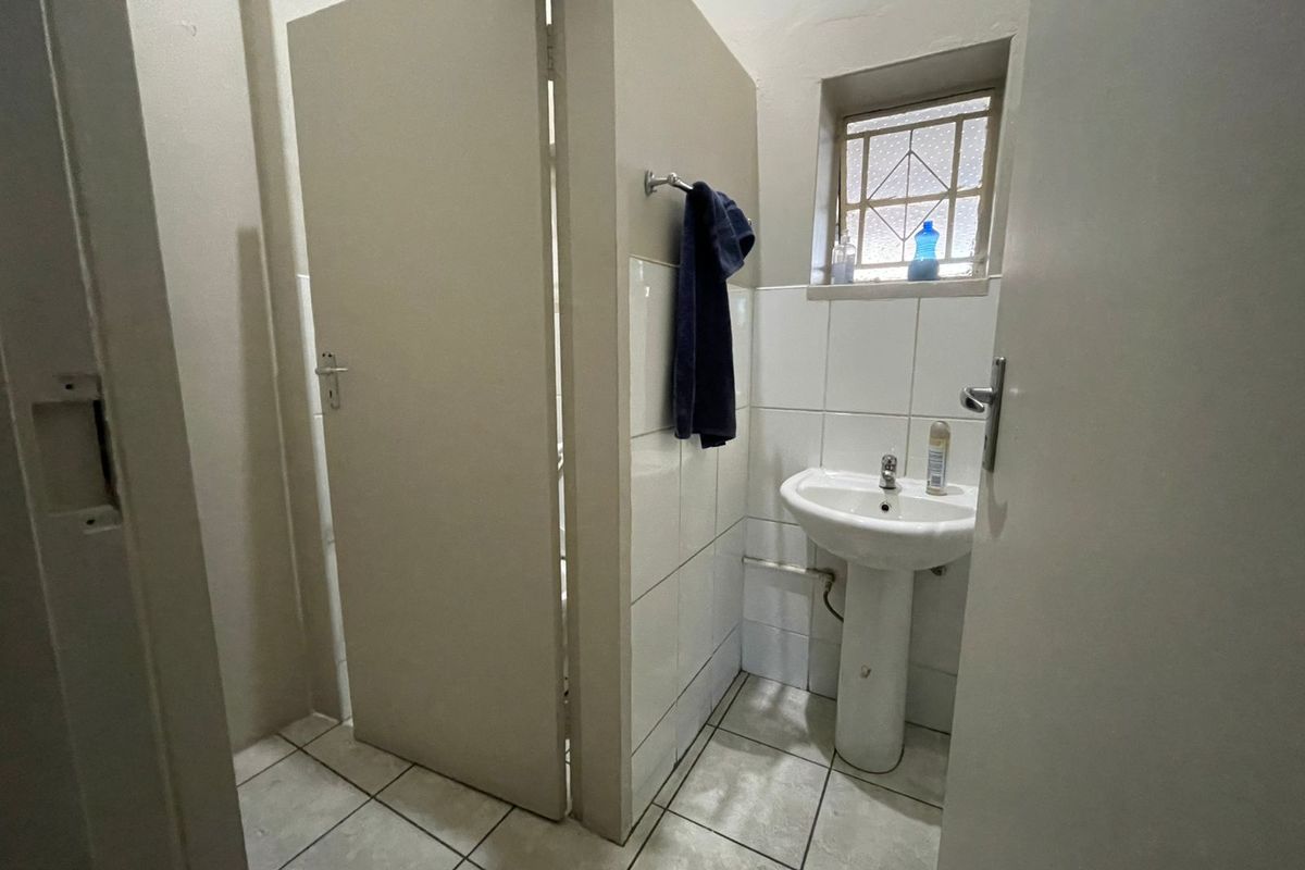 A functional industrial-style restroom featuring a pedestal basin, tiled splashback, and a separate toilet cubicle with a privacy door.