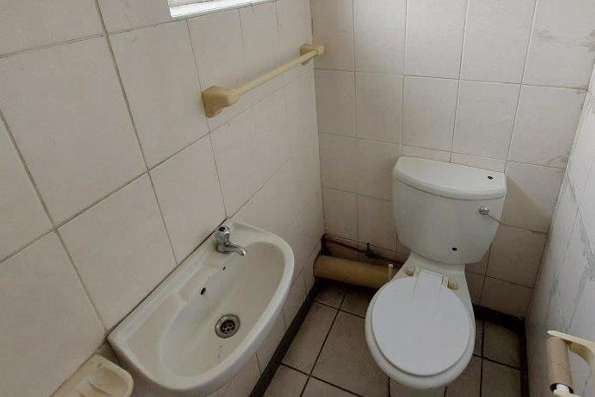 A compact guest bathroom featuring a wall-mounted basin, standard toilet, and full-height wall tiling with a small window.