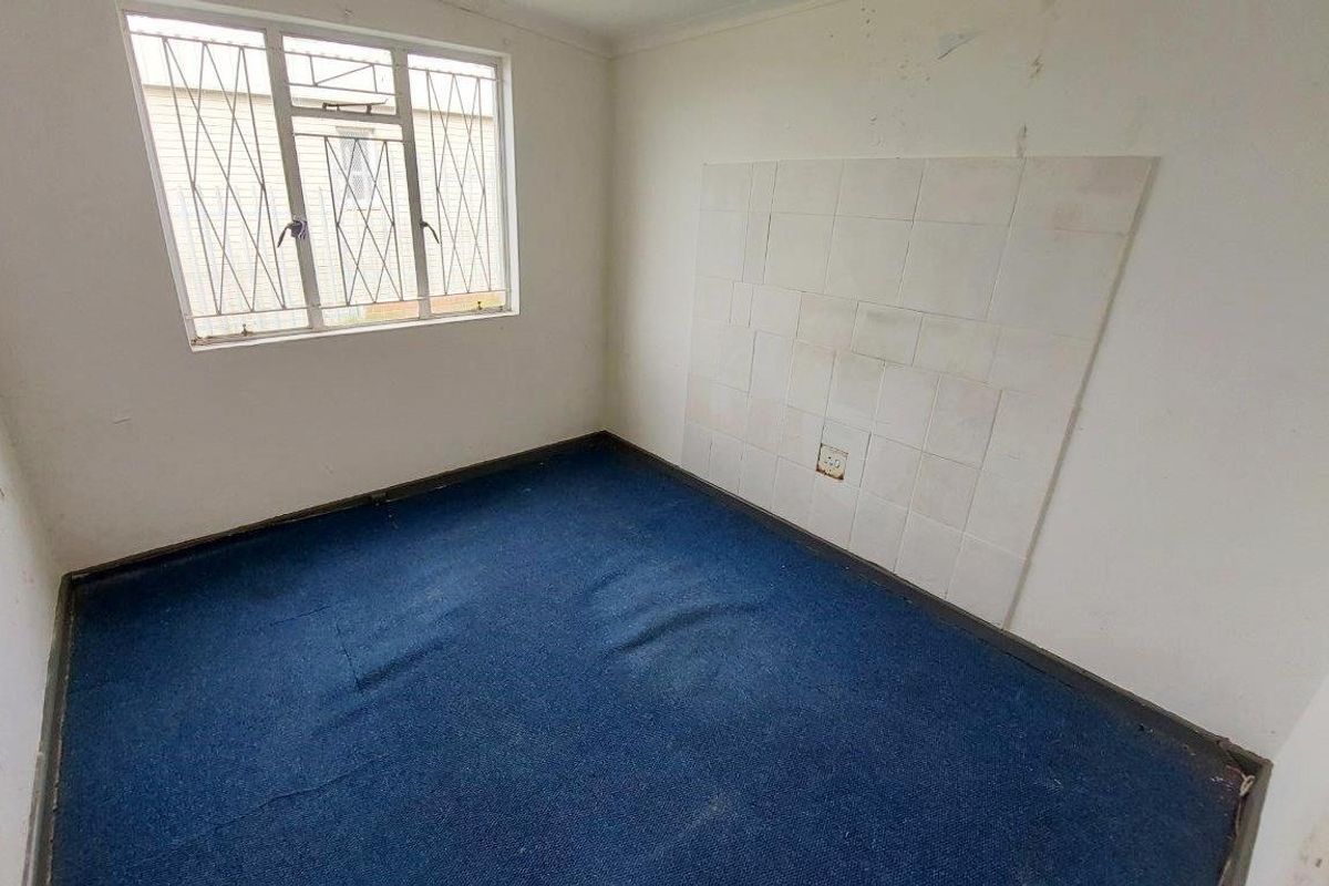 A vacant room featuring blue carpeting, a window with security bars, and a tiled section on the wall.