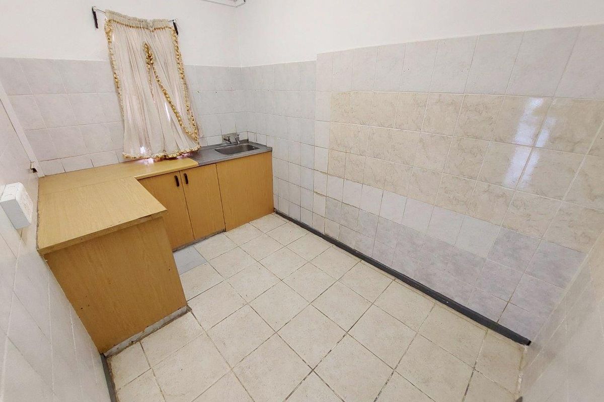A compact kitchenette area featuring basic cabinetry, a stainless steel sink, and tiled wall and floor finishes.