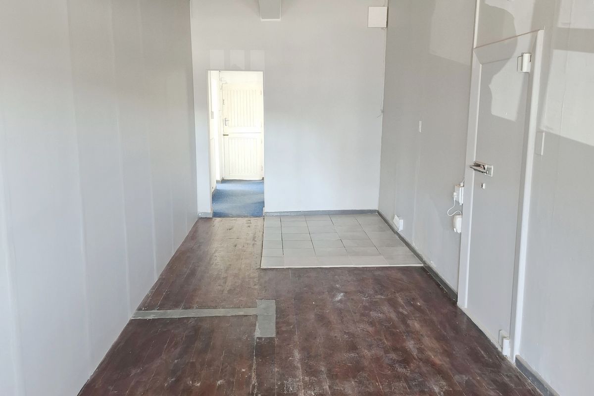 An empty retail space featuring a mix of timber and tiled flooring, neutral walls, and a central ceiling beam, ready for custom fit-out.