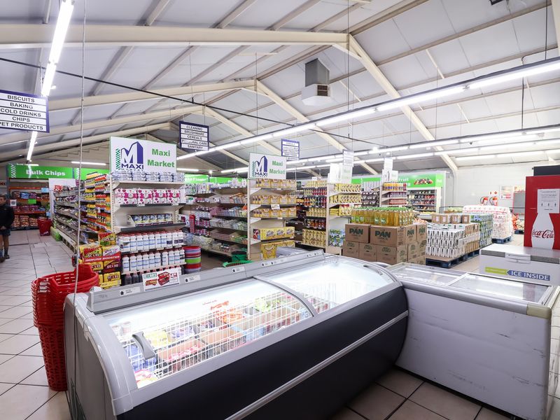 Interior view of a retail store featuring high exposed steel roof trusses, tiled flooring, and multiple commercial refrigeration units for product display.