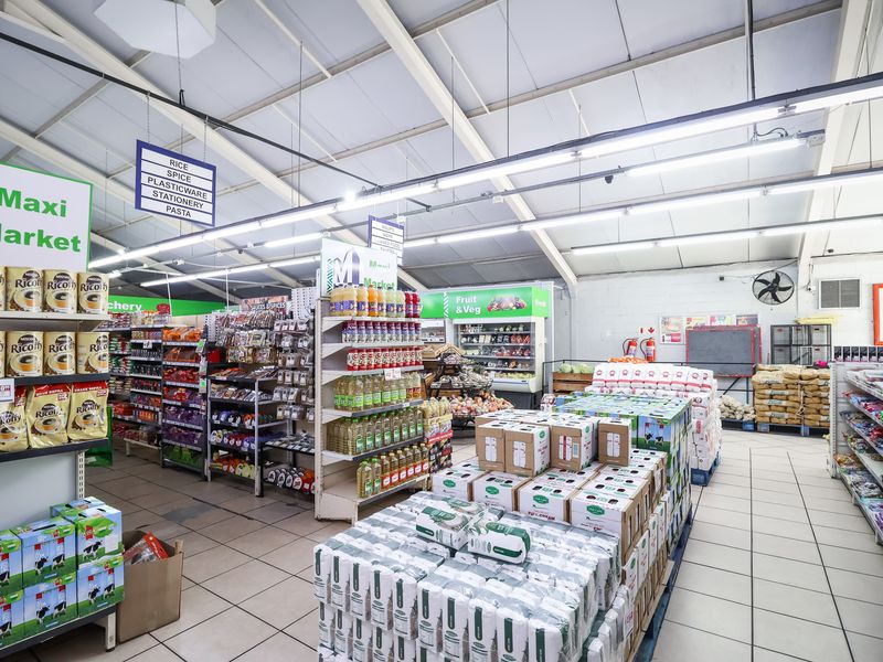Interior view of a retail market space featuring tiled flooring, exposed steel roof trusses, industrial lighting, and extensive built-in shelving for merchandise display.
