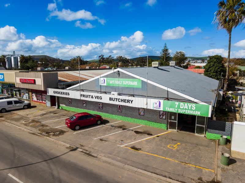 Aerial view of a retail supermarket building featuring a corrugated metal roof, paved parking area, and prominent storefront signage.