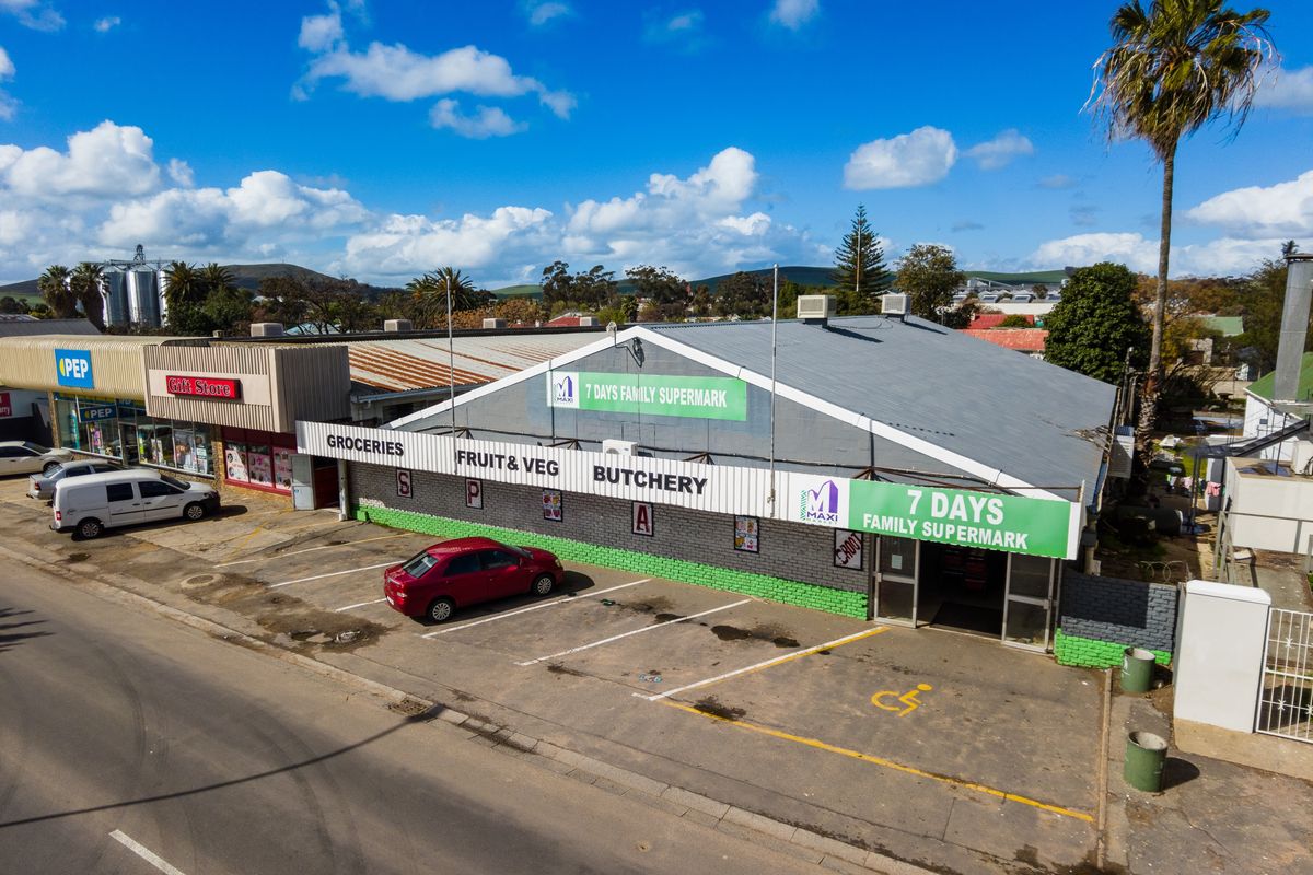 Aerial view of a retail supermarket building featuring a corrugated metal roof, paved parking area, and prominent storefront signage.