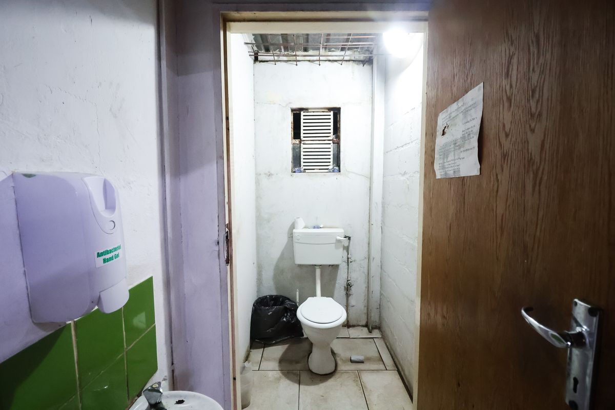 A functional bathroom facility featuring a standard toilet, tiled flooring, and a louvered window, requiring cosmetic updates to improve its overall condition.