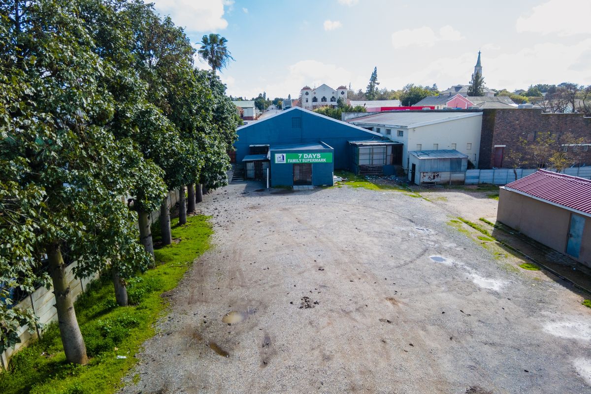 Aerial view of a commercial property featuring a large gravel parking area and a blue-painted retail building facade.