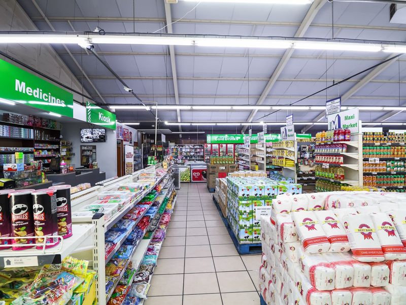 A well-organized retail store interior featuring high ceilings, fluorescent lighting, tiled floors, and extensive shelving units for various grocery and pharmacy products.