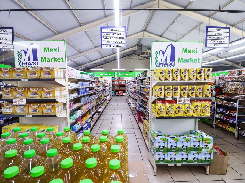 Interior view of a retail grocery store featuring organized aisles with metal shelving units, overhead fluorescent lighting, and tiled flooring.